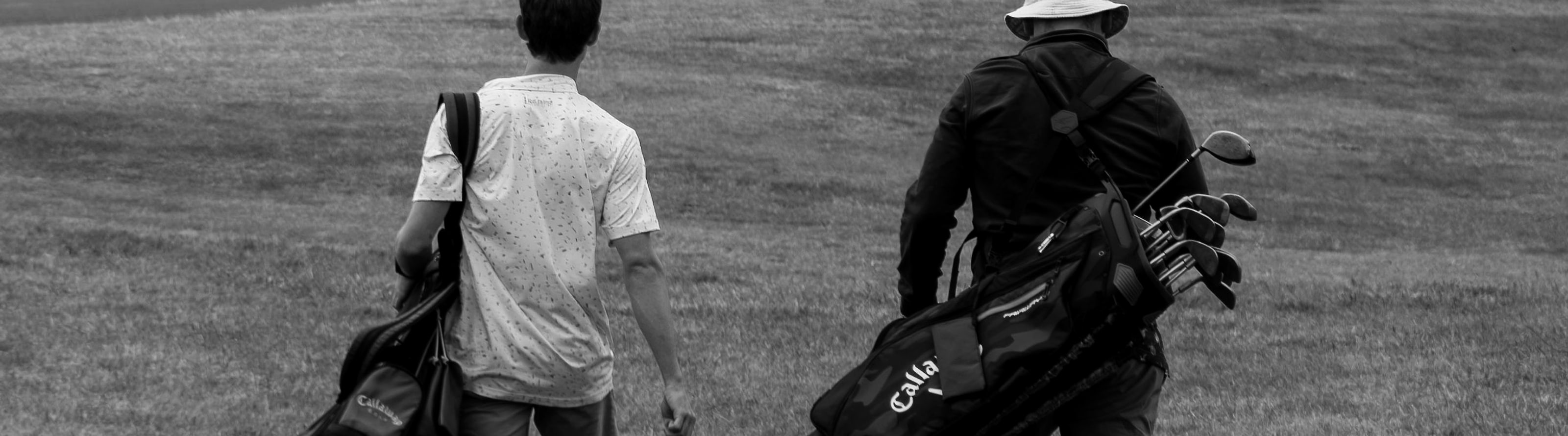 Two golfers walking a fairway with bags over their shoulders