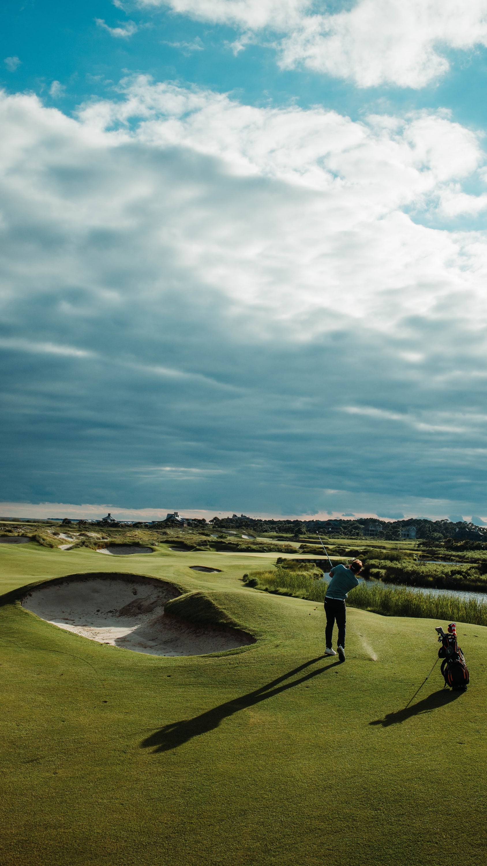 A golfer at the top of the backswing on a links fairway under a wide cloud-filled sky