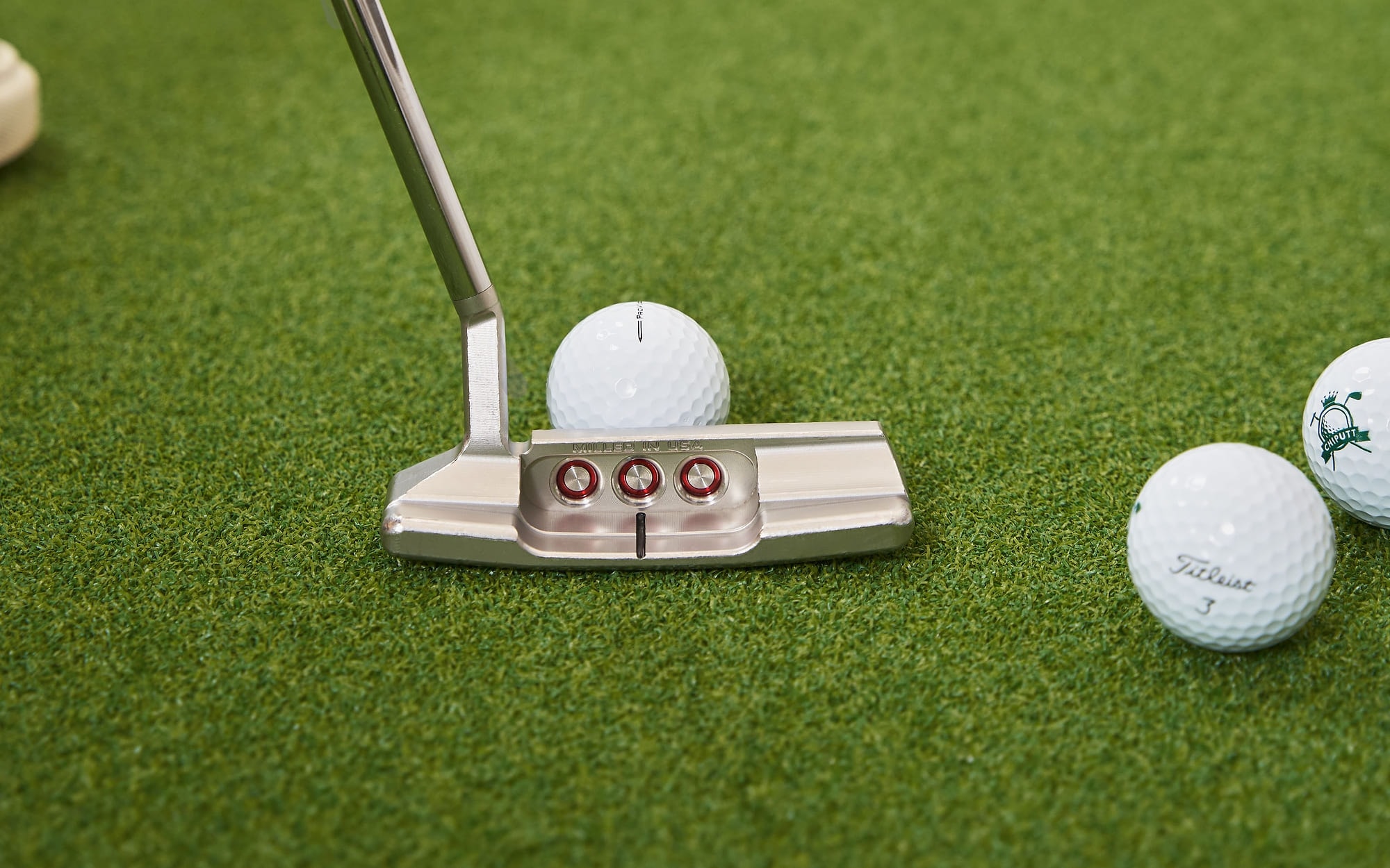 A blade putter set behind a ball on the studio mat