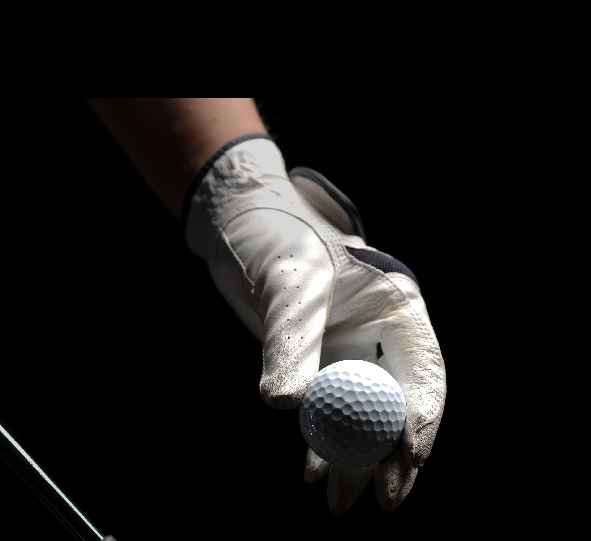 A gloved hand holding out a golf ball against a black studio background