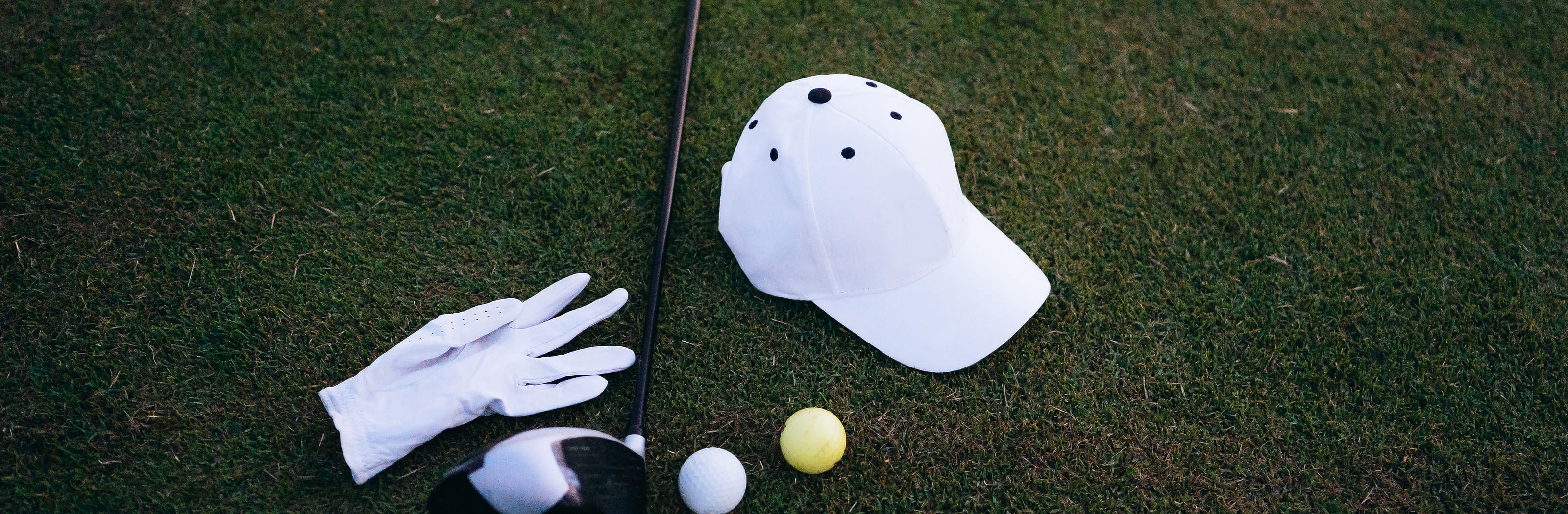 A cap, a glove and two balls lying on the grass beside a driver