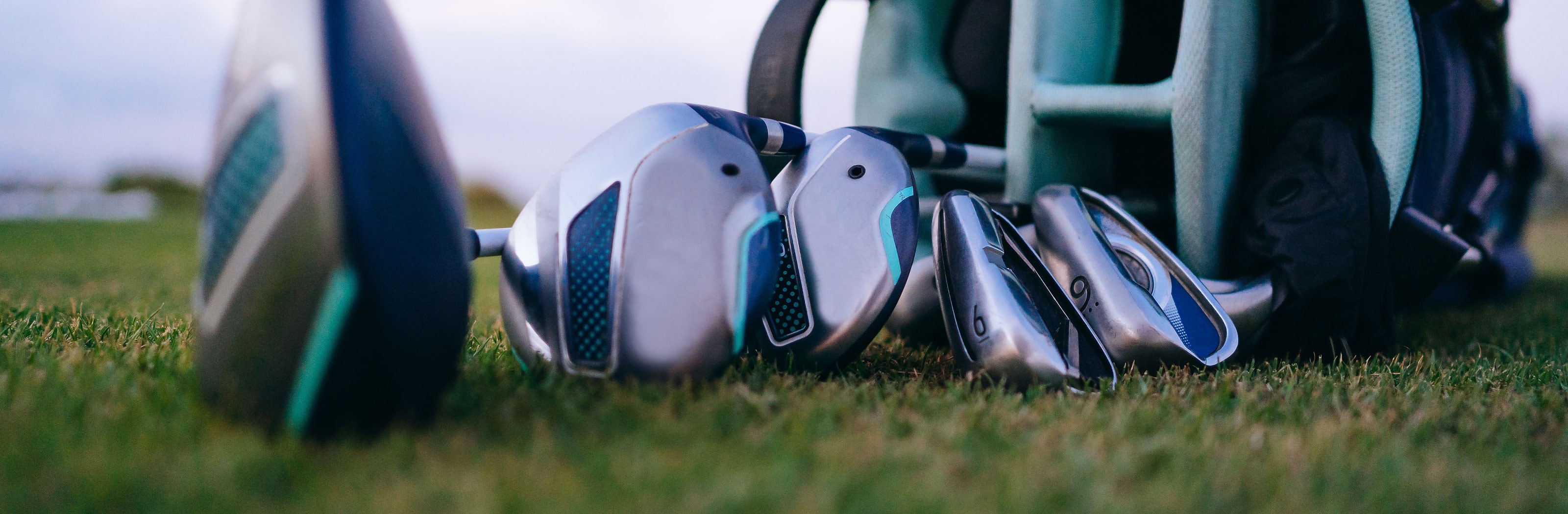 A driver and a set of irons lying on the grass beside a bag
