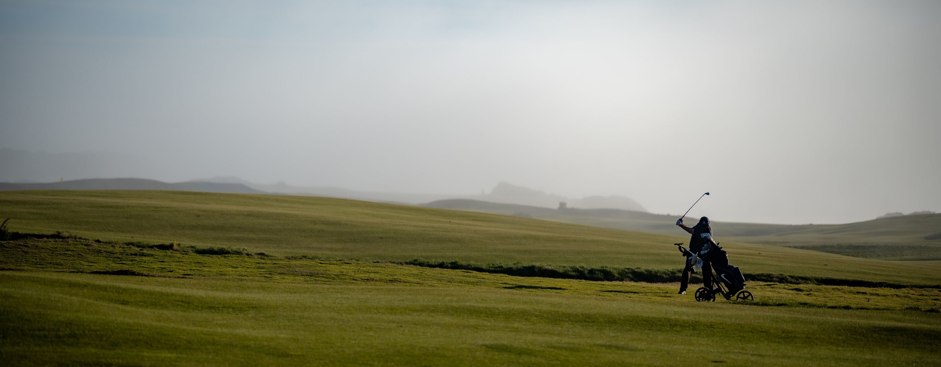 A misty links fairway with a single golfer and a trolley