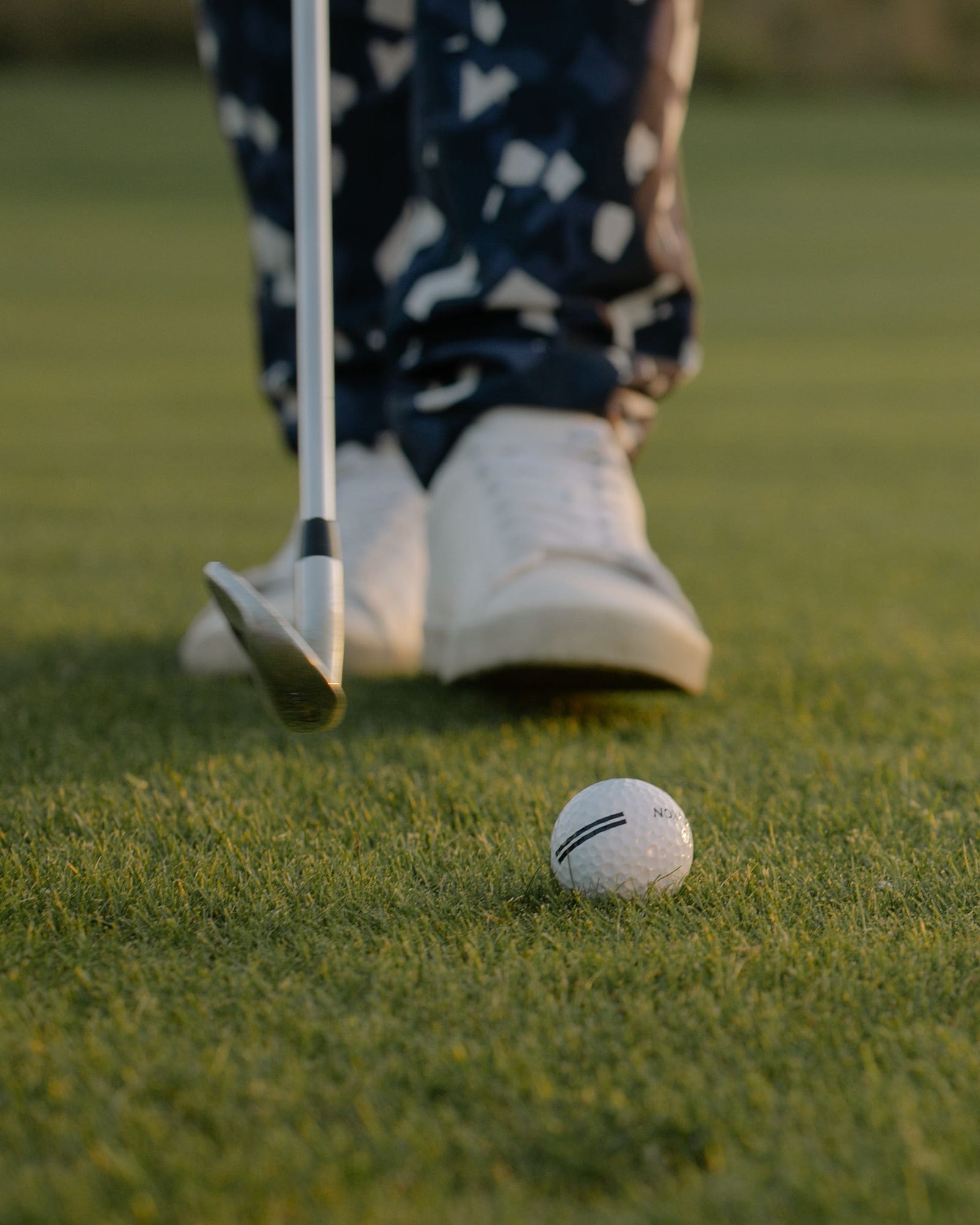 A golf shoe and a ball on the green in low evening light