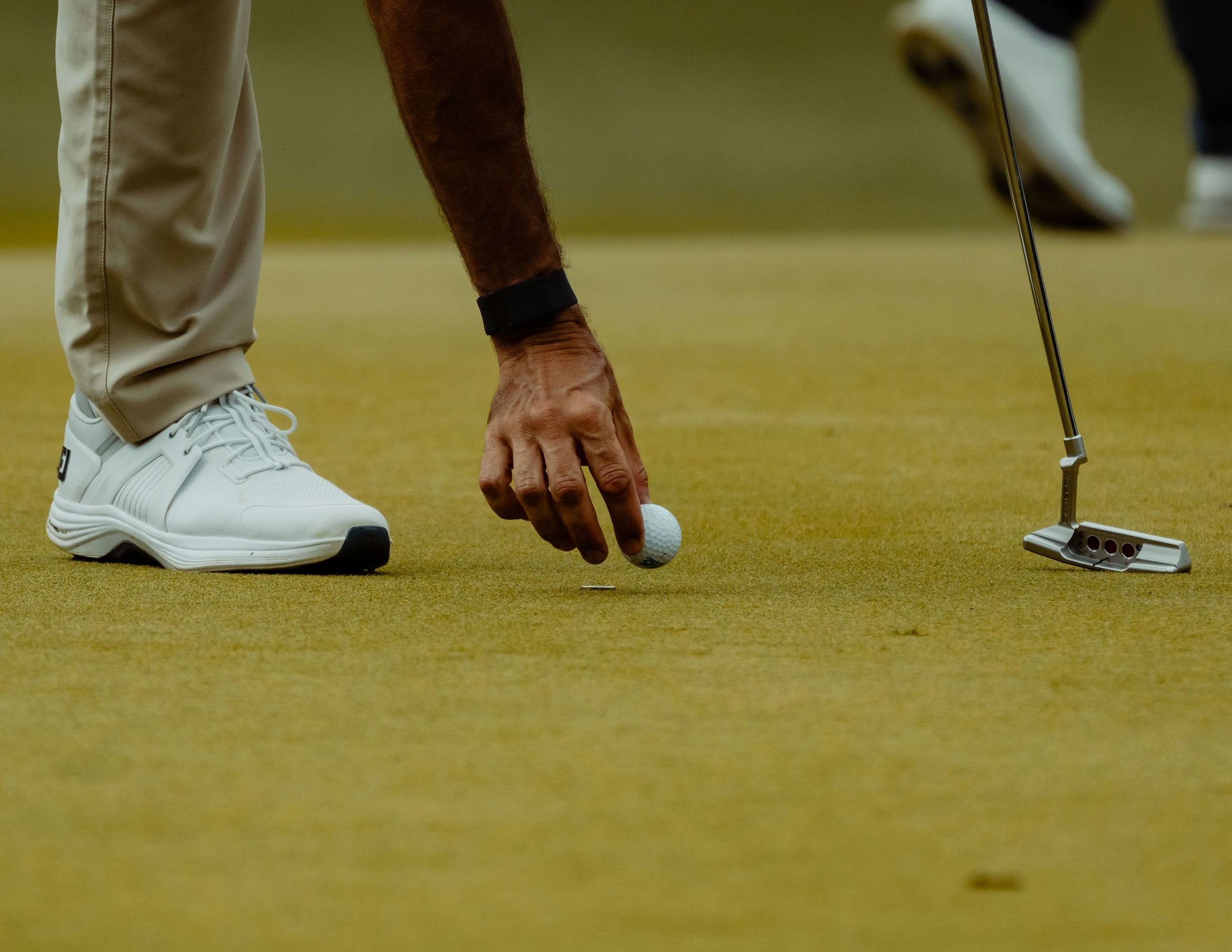 A hand placing a ball on the green beside a putter