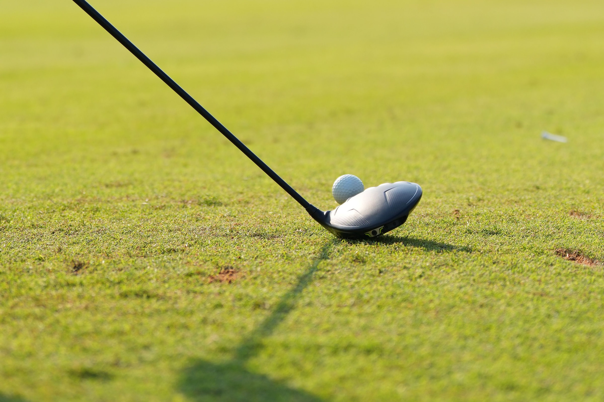 A fairway wood set behind a ball on cut grass