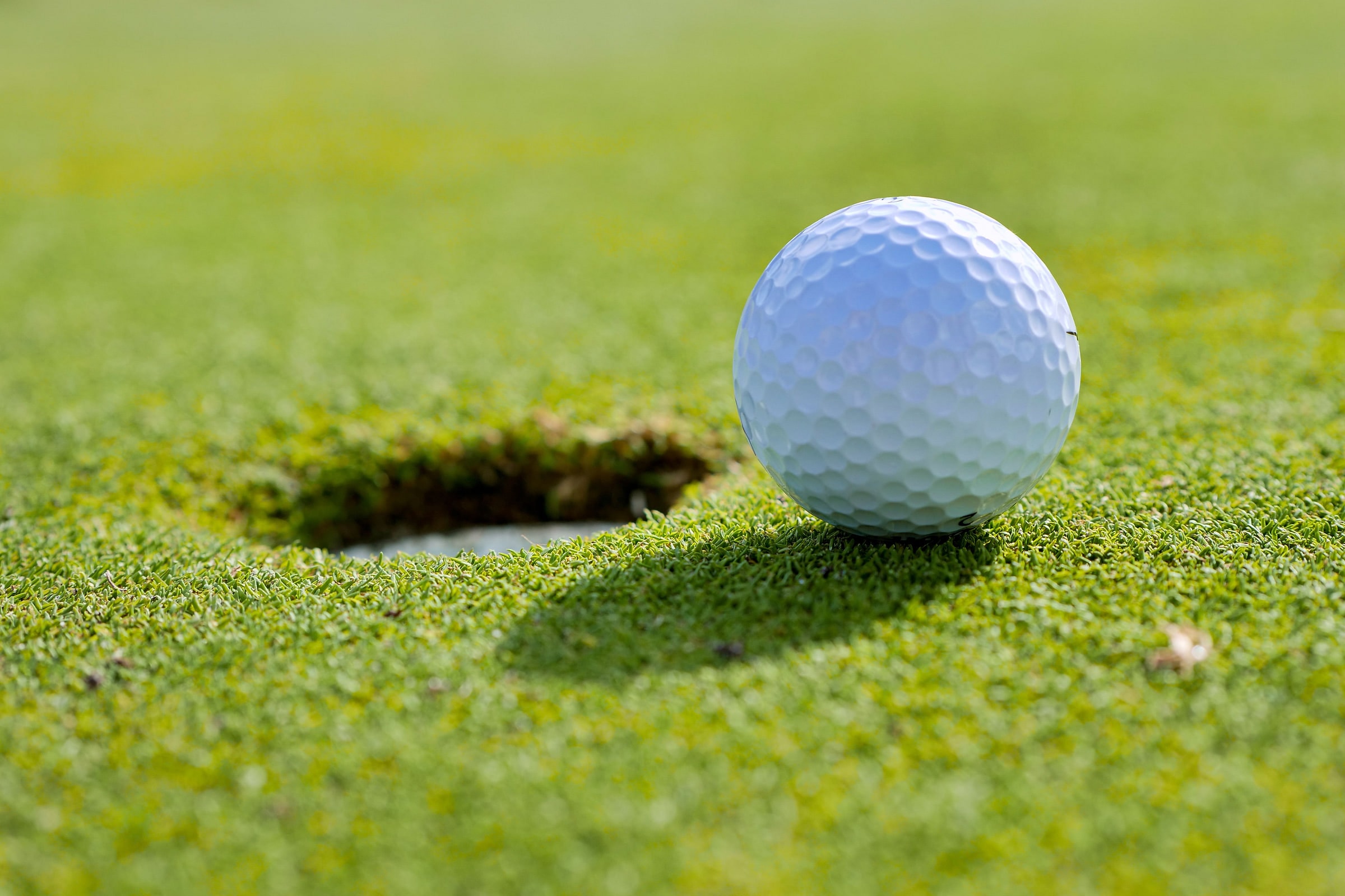 A golf ball at rest on the lip of the hole