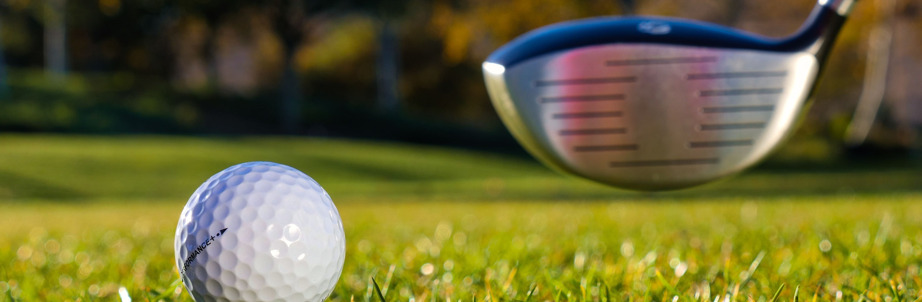 A ball teed up beside a driver face in autumn light