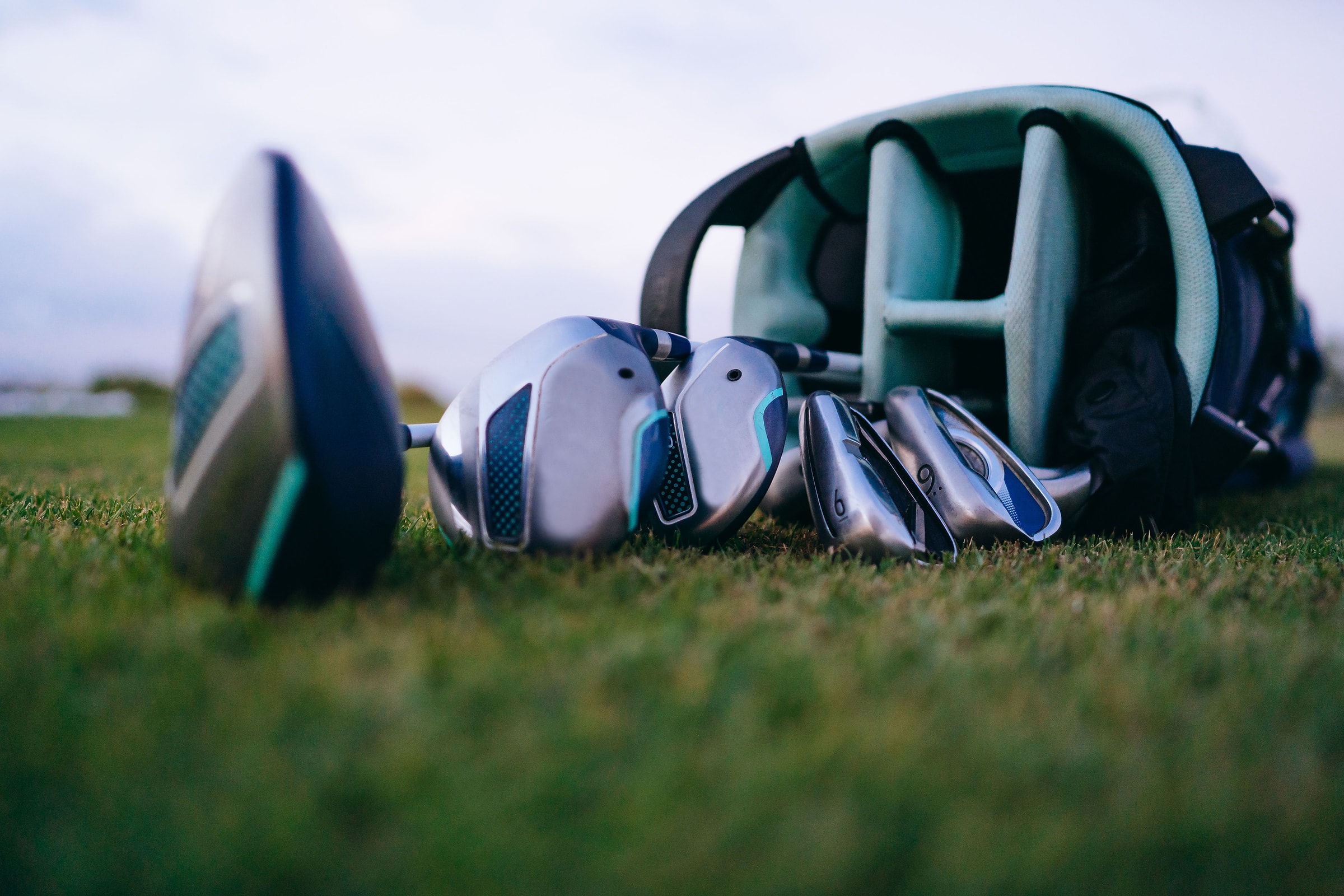 A driver and irons leaning against a stand bag on cut grass