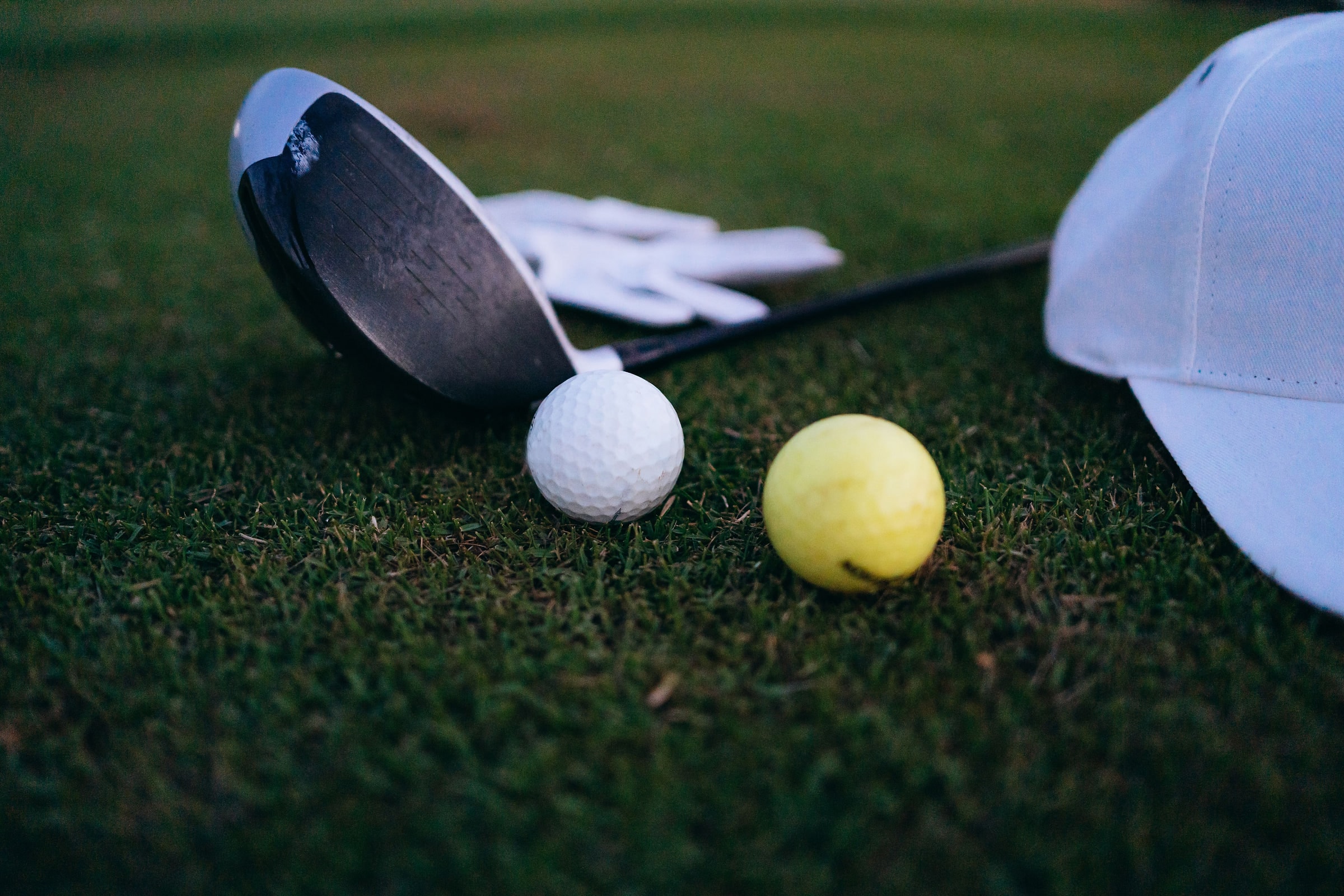 A driver head, a glove, a cap and two balls resting on cut grass