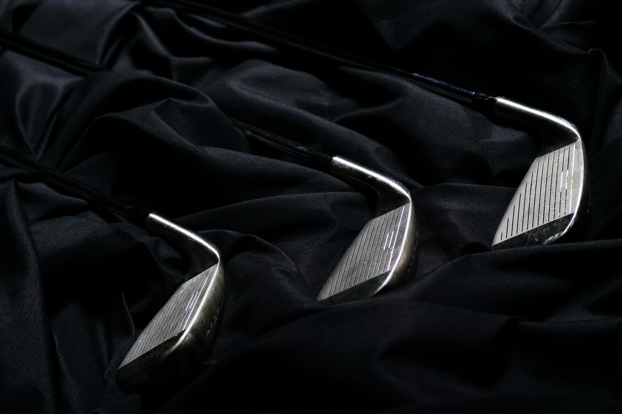 Three irons laid out on black cloth in low studio light