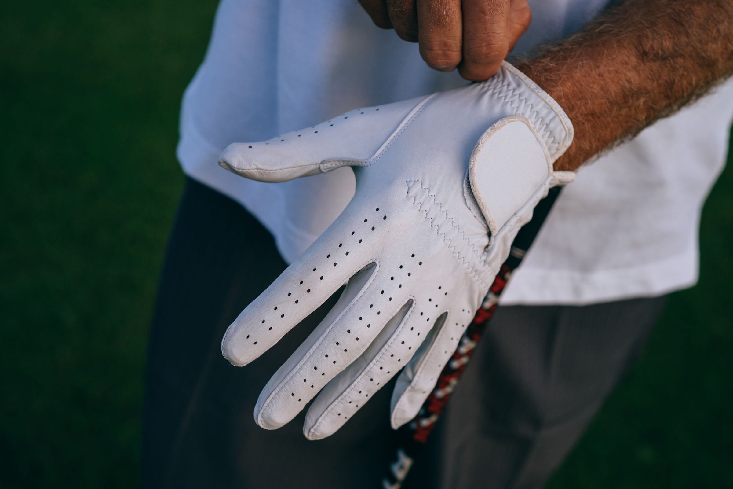 A golfer pulling a white leather glove onto their hand