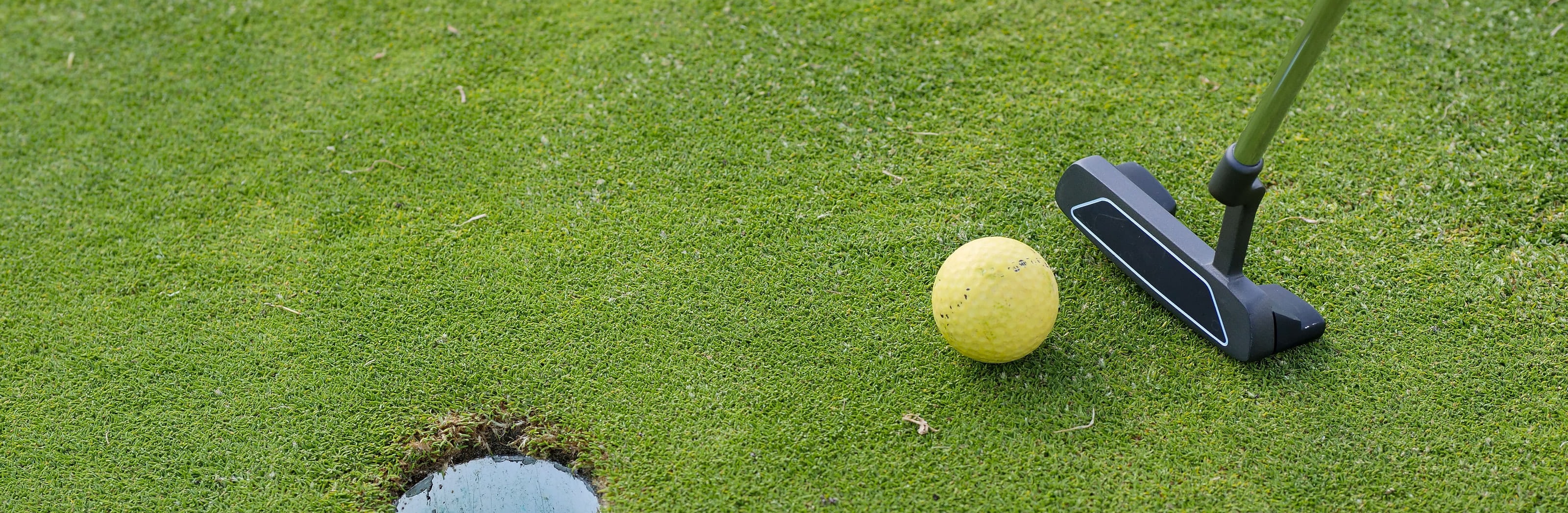 A mallet putter and a ball beside the hole on a green