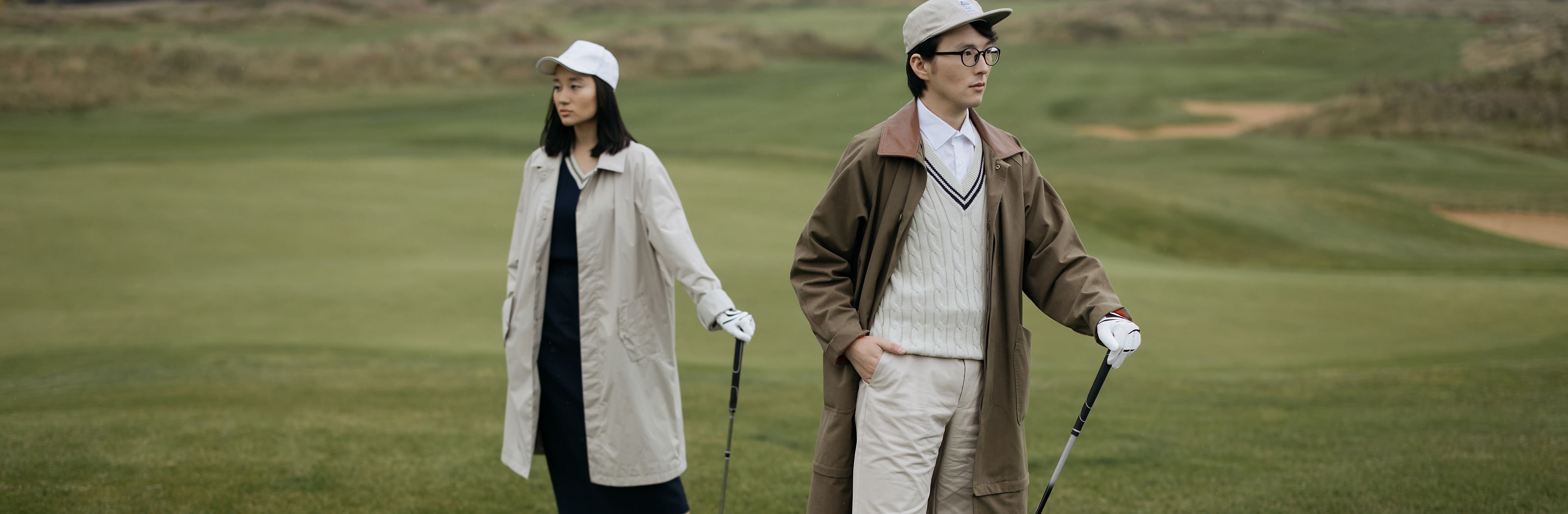Two golfers in caps and coats standing on a links fairway