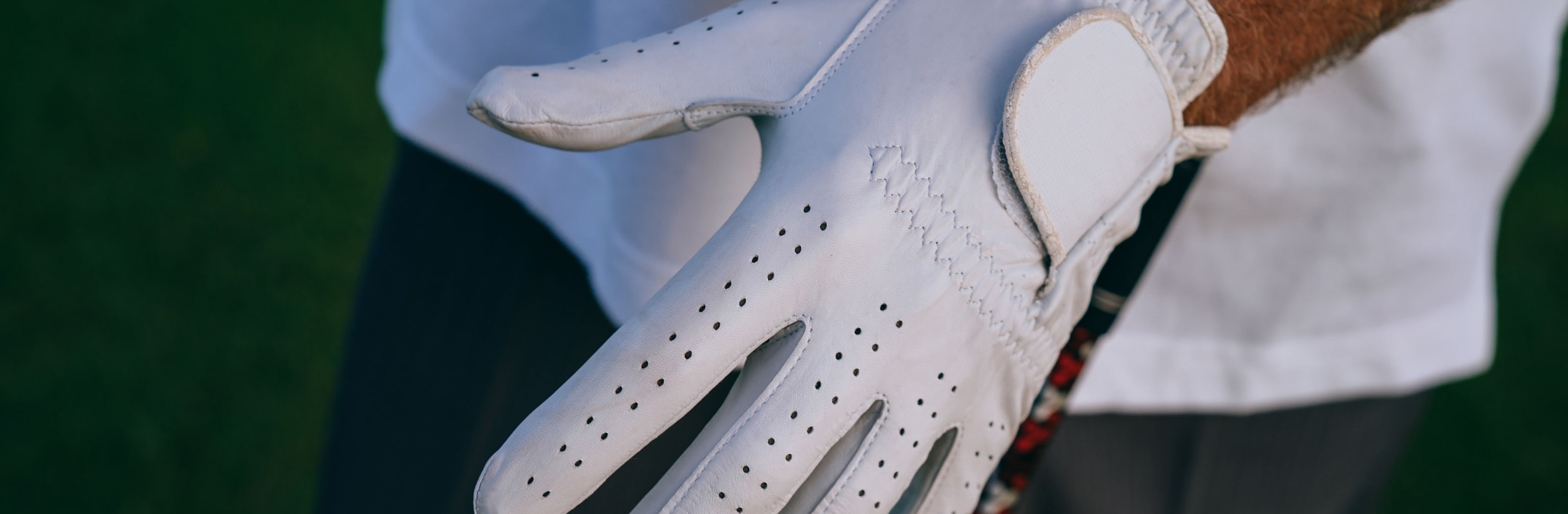 A golfer pulling a white leather glove onto their hand